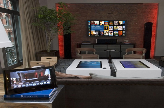 living room view of a large tv, two touch screen coffee tables and a tablet